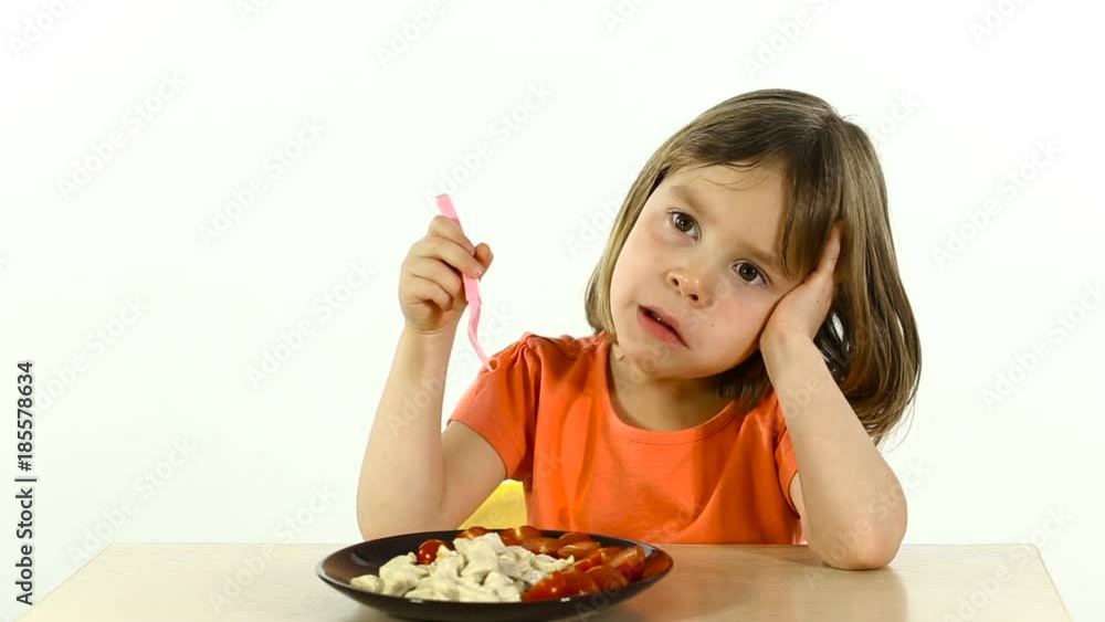 The child with obvious disgust, slowly eating food. Girl 4-5 years old, portrait on a white background. She holds a plastic plug in her hand. The child with obvious disgust, slowly eating food. Girl 4-5 years old, portrait on a white background. She holds a plastic plug in her hand.