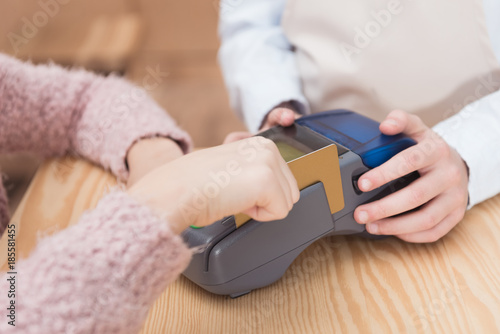 Close up of payment terminal on wooden surface and hands of girl with card
