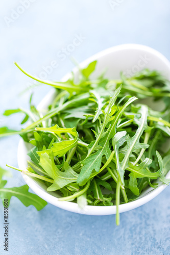 Fresh arugula leaves in bowl on table. Light background, closeup