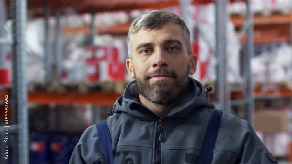 Slowmo PAN of bearded male warehouse worker walking, then taking off hard hat and looking into camera Slowmo PAN of bearded male warehouse worker walking, then taking off hard hat and looking into camera