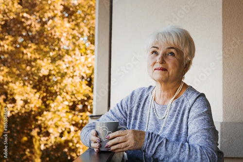 A beautiful blonde pensioner woman sitting and smiling on the terrace with a cup of tea