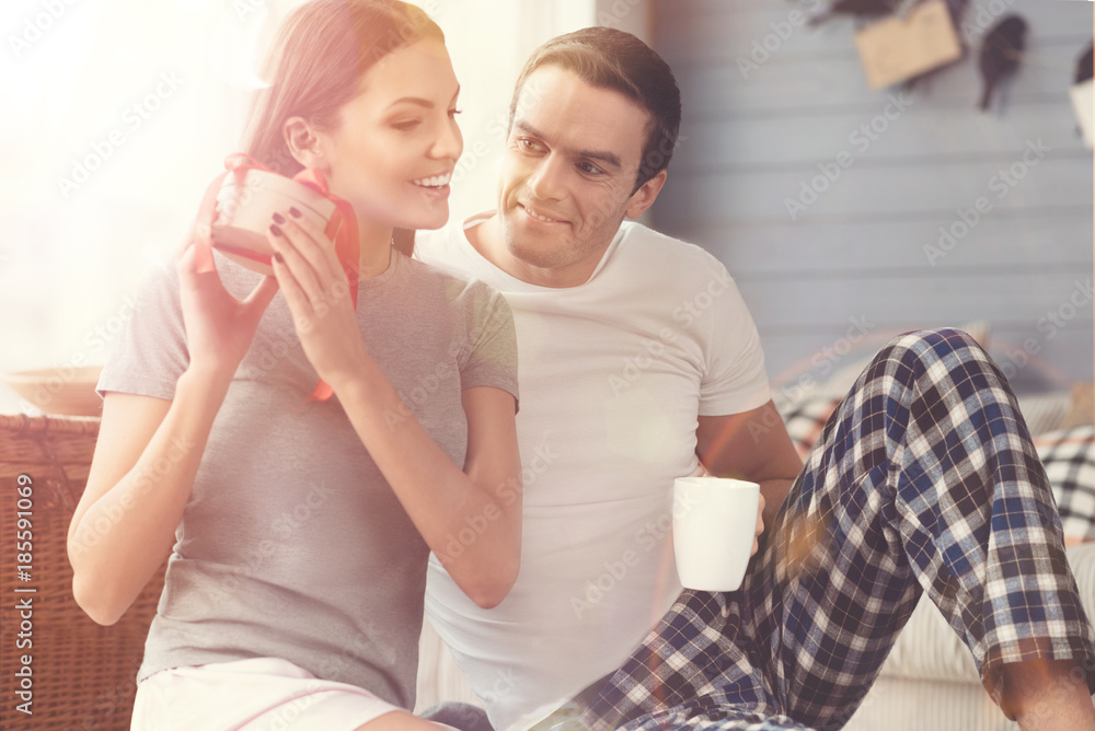 What is in there. Excited beautiful young woman shaking the present while her boyfriend looking at her and smiling What is in there. Excited beautiful young woman shaking the present while her boyfriend looking at her and smiling