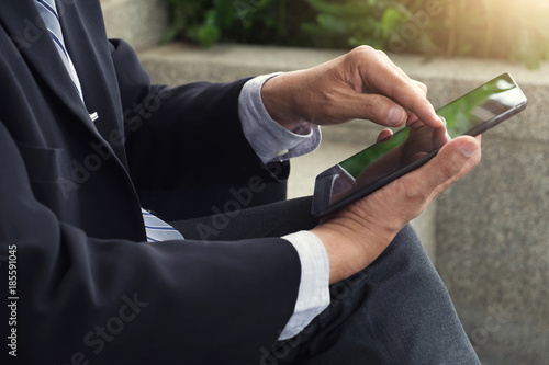 Attractive Confident businessman sitting in a black suit and using digital tablet to analyze investment and checking account