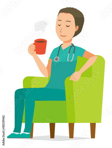 A male doctor wearing a green scrub sits on the sofa and is drinking coffee