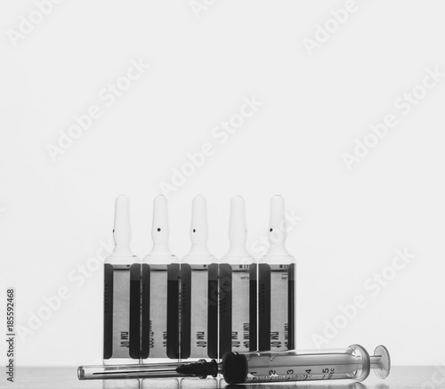 the ampoules with solution for injections and disposable syringe on agrey background with space for text, black and white photo