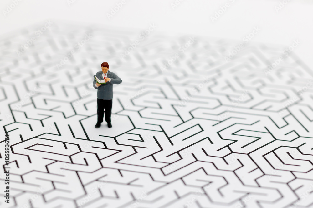 Miniature people: Businessman reading on center of maze. Concepts of finding a solution, problem solving and challenge. Miniature people: Businessman reading on center of maze. Concepts of finding a solution, problem solving and challenge.