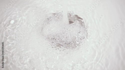 Slow motion bubbles of clear clear water in a silvery drain hole of a white bath or sink