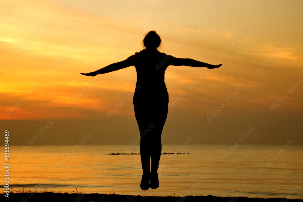 Silhouette of happy carefree woman jumping on the beach under in the sunrise time. Relax, freedom and feel free on vacation time. Healthy living with Summer sport and freedom concept Silhouette of happy carefree woman jumping on the beach under in the sunrise time. Relax, freedom and feel free on vacation time. Healthy living with Summer sport and freedom concept