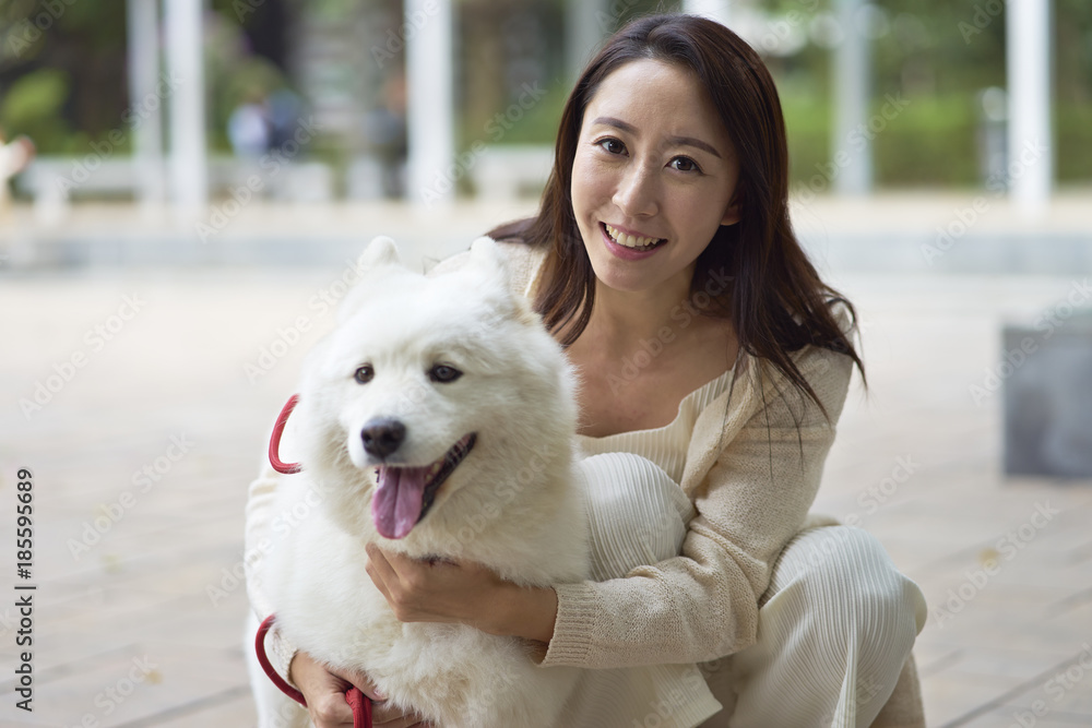 Asian beauty embracing her dog smiling at camera outdoor in garden