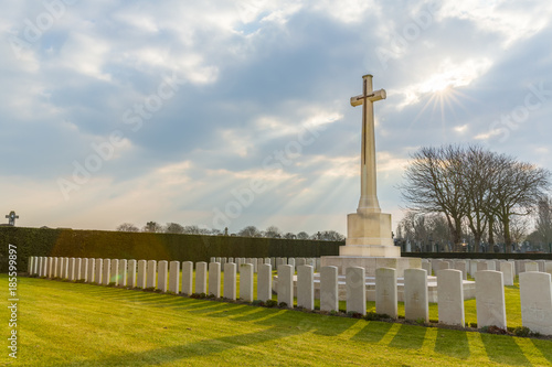 Fotografie Cross and Gravestones at the DUNKIRK MEMORIAL CEMETARY, Dunkerque, France with Sun Rays in the cloudy sky