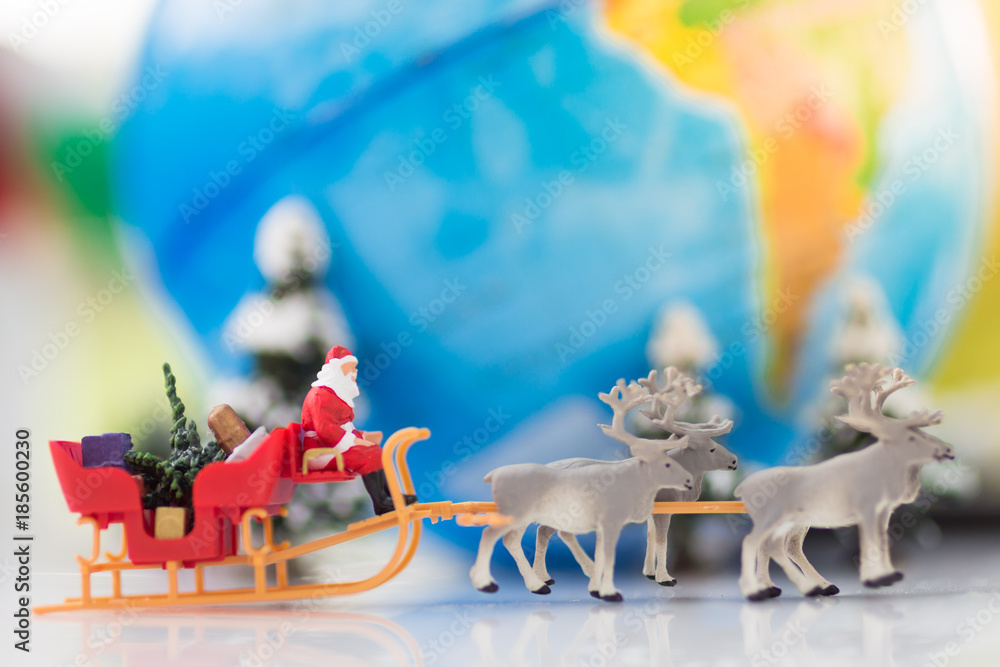 Miniature Santa Claus drive a wagon with a reindeer during the snowfall on world map. Using as concept in Christmas day.