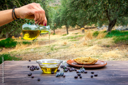 Vászonkép Bottle pouring cretan extra virgin olive oil in a bowl on wooden table at an olive tree field, Greece