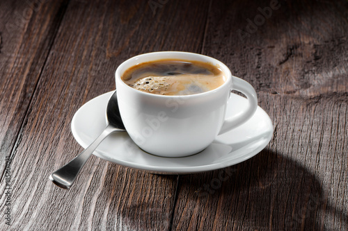 cup of coffee with nice foam close-up,  spoon and white saucer on dark wooden background
