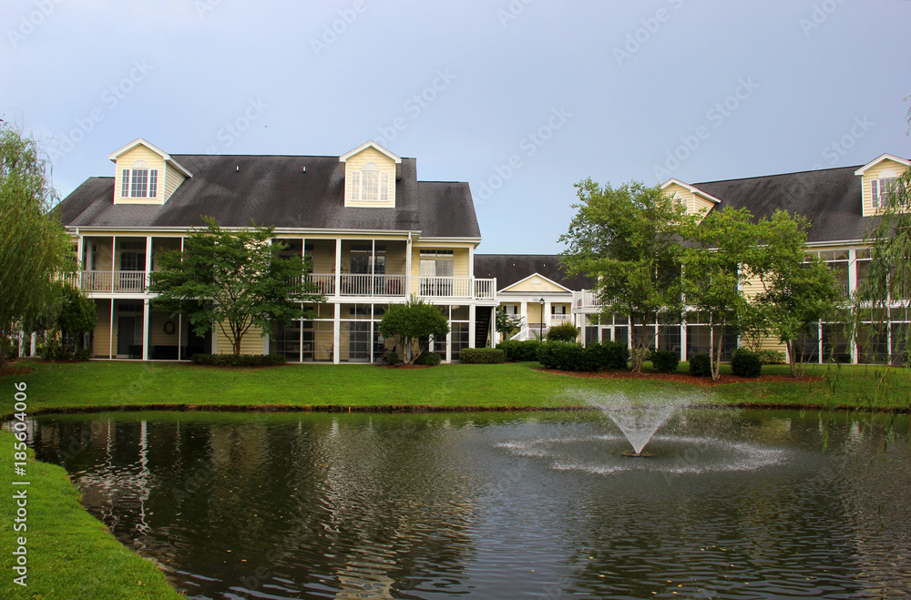 Southern modern architecture and vacation rentals background. Myrtle Beach suburb morning view with buildings around the pond with sprinkling fountain. South Carolina, USA. Southern modern architecture and vacation rentals background. Myrtle Beach suburb morning view with buildings around the pond with sprinkling fountain. South Carolina, USA.