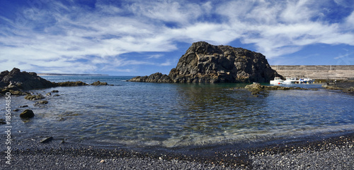 Meeresküste mit Fels und kleinem Hafen.
