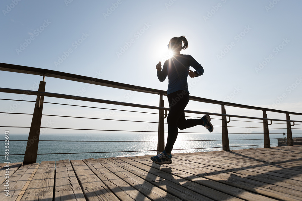 sporty fitness female runner running on seaside boardwalk