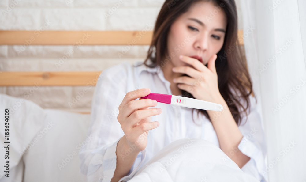 Selective focus Pregnancy test positive result on hand of woman ,have morning sickness pregnant woman on bed in her bedroom . Selective focus Pregnancy test positive result on hand of woman ,have morning sickness pregnant woman on bed in her bedroom .