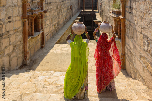 Women carry ceramic pot in step well