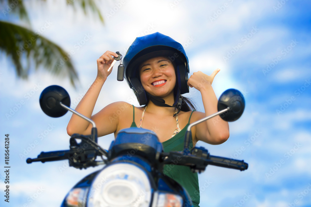 Naklejka premium pretty Asian Chinese girl showing key of new motorbike wearing motorcycle safety helmet smiling proud in scooter buying and rental
