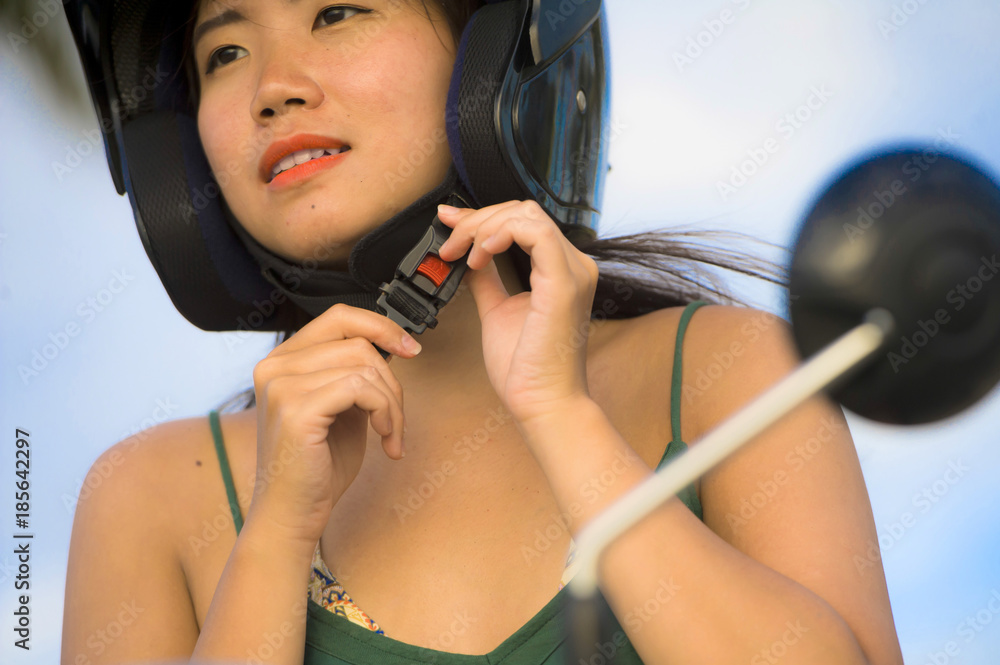Obraz premium young pretty happy and cute Asian Chinese woman adjusting motorcycle helmet riding on scooter motorbike isolated on a blue sky in safety concept