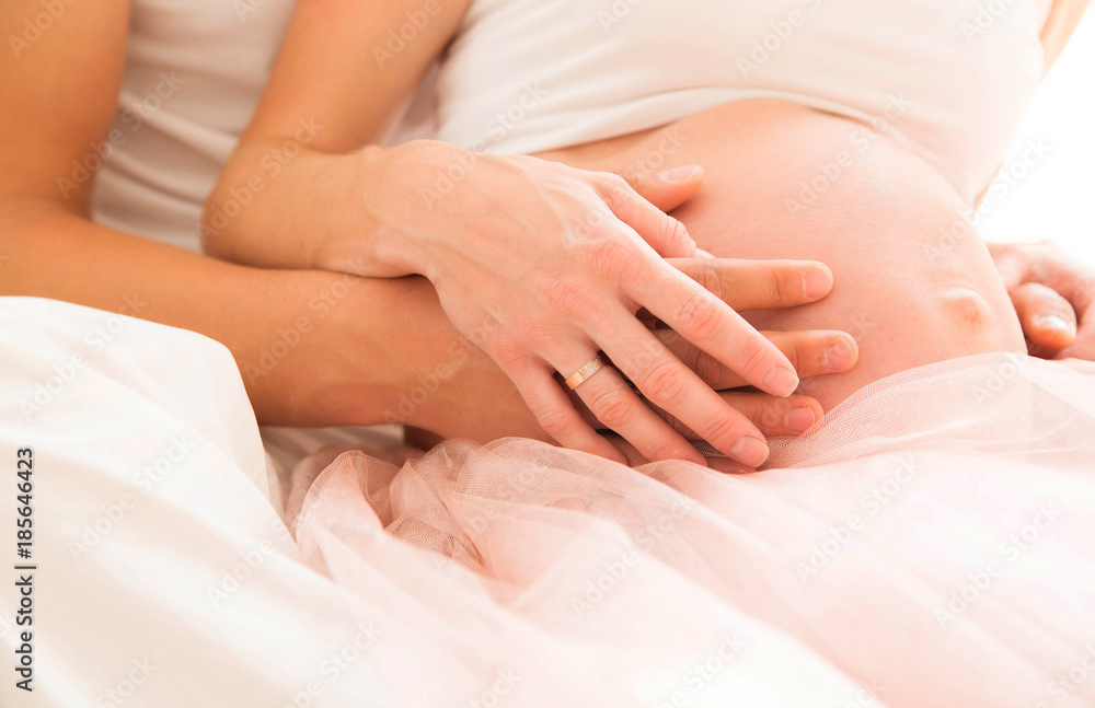 two pairs of hands on the bare belly of a pregnant woman