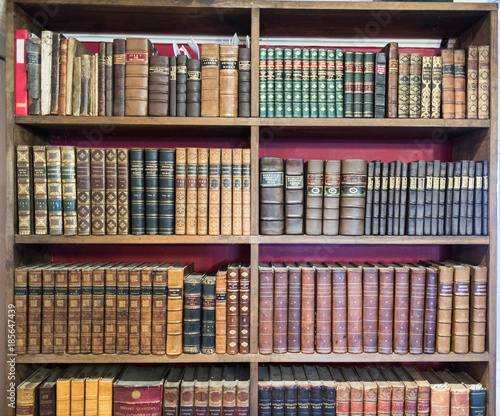 Rows of leather bound books on shelves in a home library 