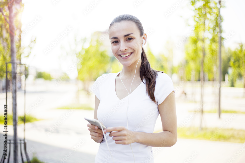 Gorgeous beautiful young woman messaging on the smart-phone at the city street background and looking on camera Gorgeous beautiful young woman messaging on the smart-phone at the city street background and looking on camera