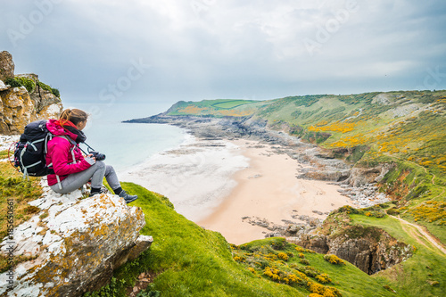 Female Backpacker Looking Into Distance At Rocky Sea Shore In Rhossili, Wales Coast Path photo
