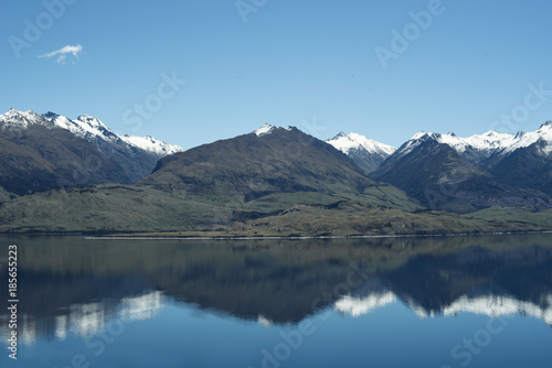 Paisaje de monta  as frente a un gran lago donde se reflejan. Cielo azul despejado.