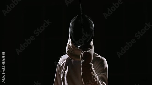 A man dressed for fencing wears a mask and is preparing a rapier. Close-up. The position to start sparring photo