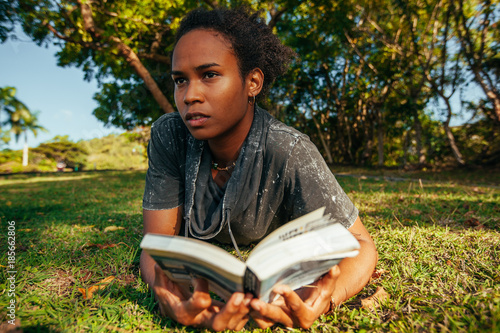 Obraz na plátně Beautiful young woman with afro hairstyle and book in her hands lying on the gra