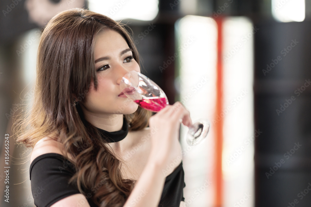 Portrait of a smiling young woman holding a glass of sparkling rose wine. Pretty chinese single woman holding alcoholic beverages with real open air dance club in background. Party concept.