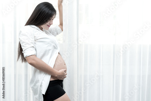 Healthy chinese motherhood concept. Portrait of young Chinese pregnant woman at her home and touching her tummy. Taken indoor with real six months old pregnant woman. Free Download Healthy chinese motherhood concept. Portrait of young Chinese pregnant woman at her home and touching her tummy. Taken indoor with real six months old pregnant woman. - GFXLoad