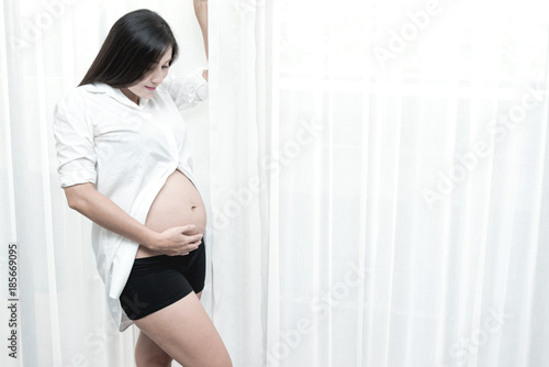 Healthy chinese motherhood concept. Portrait of young Chinese pregnant woman at her home and touching her tummy. Taken indoor with real six months old pregnant woman. Free Download Healthy chinese motherhood concept. Portrait of young Chinese pregnant woman at her home and touching her tummy. Taken indoor with real six months old pregnant woman. - GFXLoad