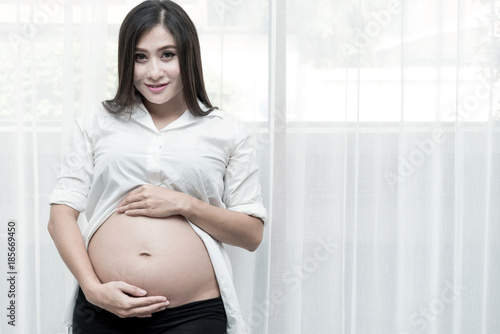 Healthy chinese motherhood concept. Portrait of young Chinese pregnant woman at her home and touching her tummy. Taken indoor with real six months old pregnant woman. Free Download Healthy chinese motherhood concept. Portrait of young Chinese pregnant woman at her home and touching her tummy. Taken indoor with real six months old pregnant woman. - GFXLoad