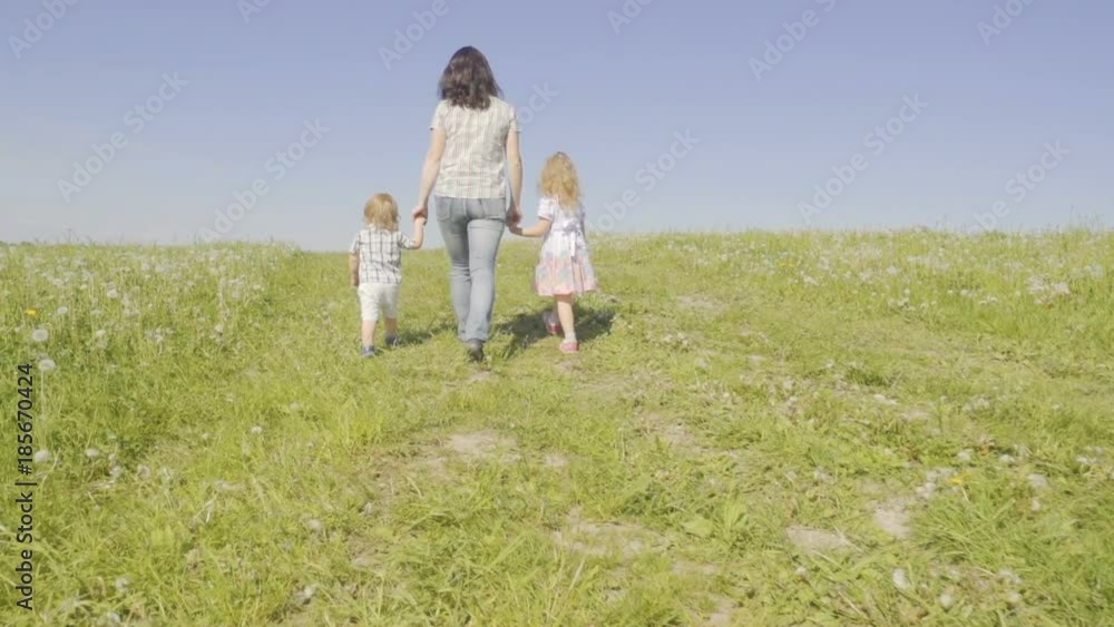 Family mother with her son and daughter are walking around the field. Walk in the fresh air. Summer sunny day. Slow Motion. Family mother with her son and daughter are walking around the field. Walk in the fresh air. Summer sunny day. Slow Motion.