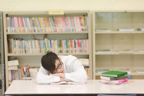 Young student study hard in library. Asian male university student doing study research in library and fall to sleep with books and on desk and smiling. For back to school education concept.
