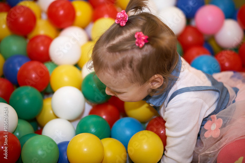 Happy little kid girl play in the playing room pool full of colorful balls. Funny child having fun indoors. Birthday party
