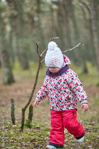 Little girl wear jacket and hat walk is playing at the forest near baltic sea on cloudy sky in winter time.