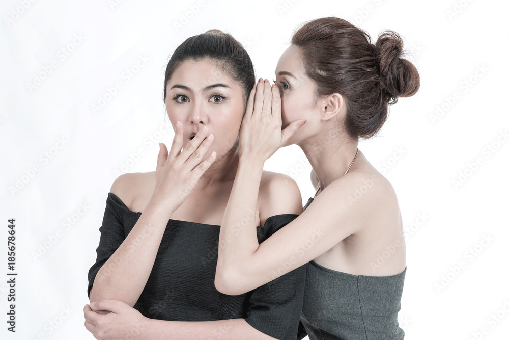 Beauty women gossip concept. Portrait of two beautiful young Chinese Asian Oriental women isolated in white. Whispering to her ears for a shocking news, studio shot.