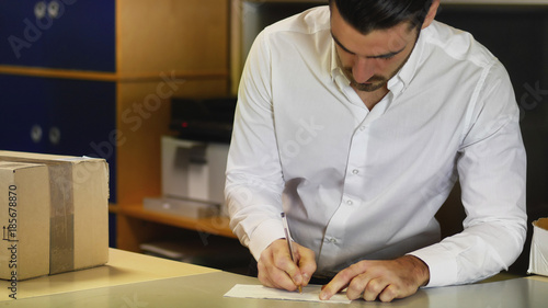 Businessman standing at office desk and looking at parcel delivered to him by courier.