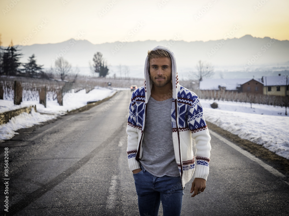 Handsome young man outdoor in winter fashion wearing black coat and woolen scarf in snow environment on a country road Stock Adobe Stock
