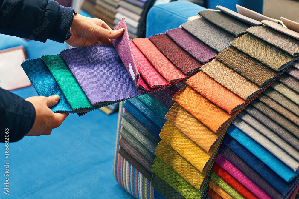 Young woman is making her decision while choosing a color of a fabric from a huge variety in a shop