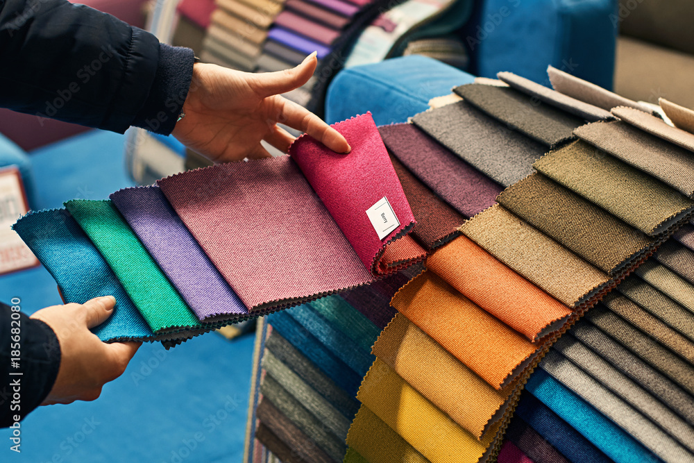 Young woman is making her decision while choosing a color of a fabric from a huge variety in a shop - obrazy, fototapety, plakaty 