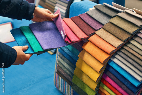 Obraz na płótnie Young woman is making her decision while choosing a color of a fabric from a huge variety in a shop w salonie