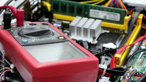 Red  multimeter for repair equipment, selective focus with shallow depth of field. Measurement of the voltage in the motherboard.
