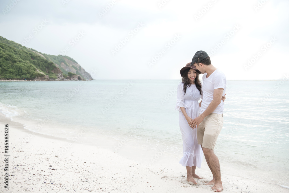 Couple holding each other on beach. Young happy interracial couple on beach holding each other. Asian woman, Caucasian man. Young mixed race romance concept.