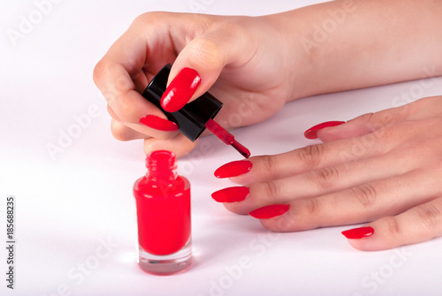 Woman painting her nails on finger in red color on white background