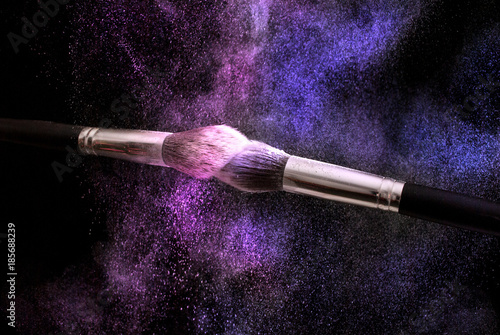 Two make up brushes and pink and purple powder explosion dust, selective focus, close up