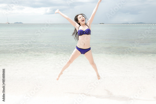 Beautiful young single chinese woman having fun on beach. Jumping, wearing bikini.